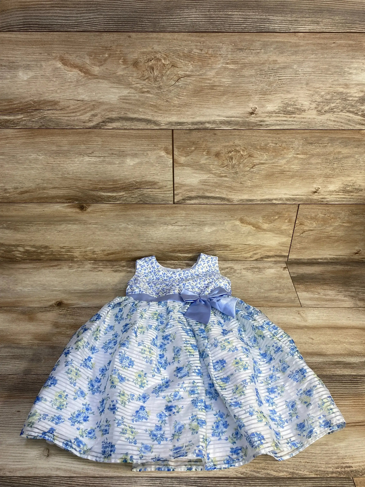 Top down view of blue floral sleeveless toddler dress size 3T with satin waist bow and full skirt on wood background