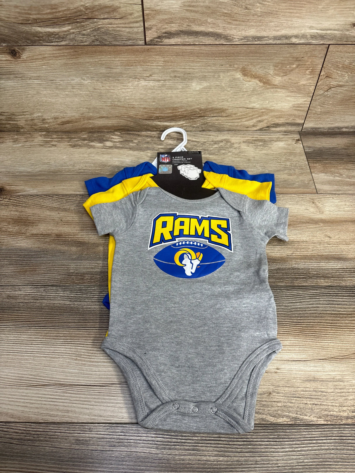 Gray and yellow Rams baby bodysuit on hanger, football team logo, wooden floor background