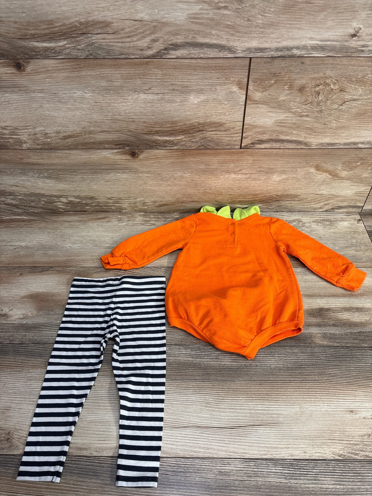 Orange dinosaur-themed baby onesie with green spikes paired with black and white striped leggings on wood floor