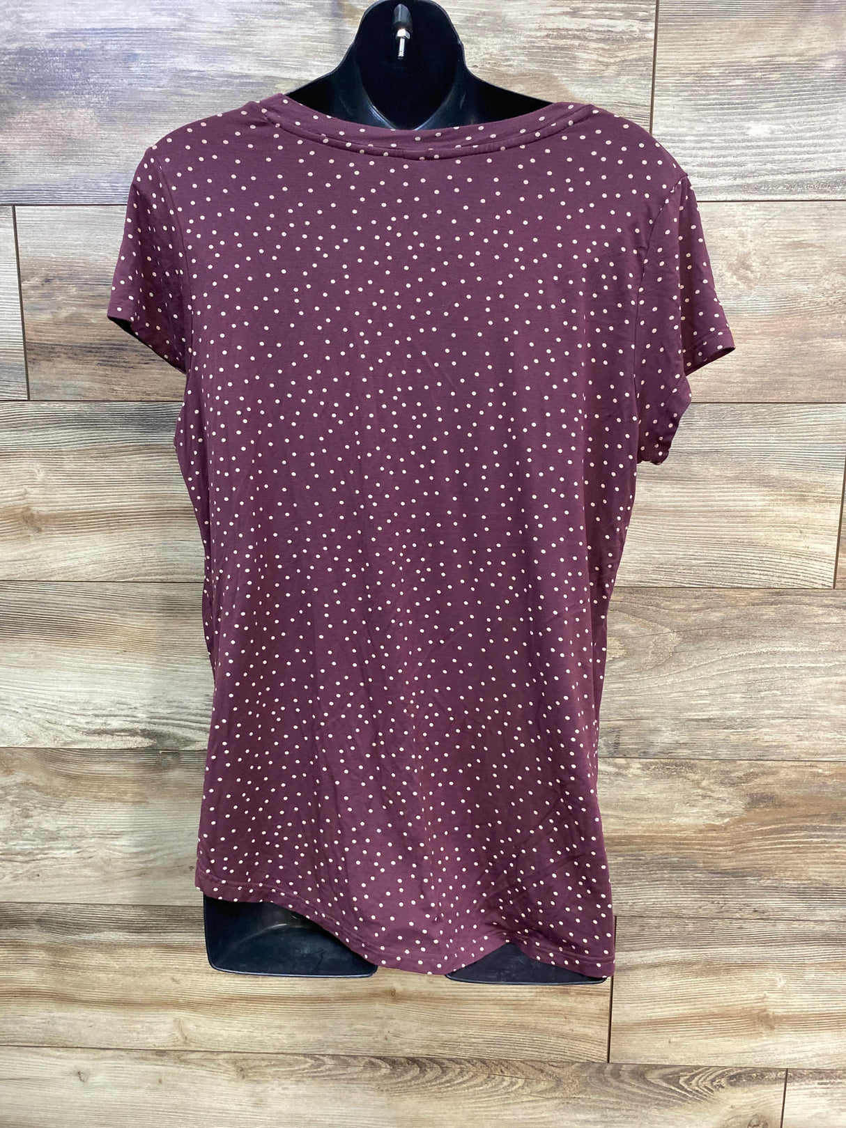 Maroon short sleeve polka dot shirt on black mannequin against wood background