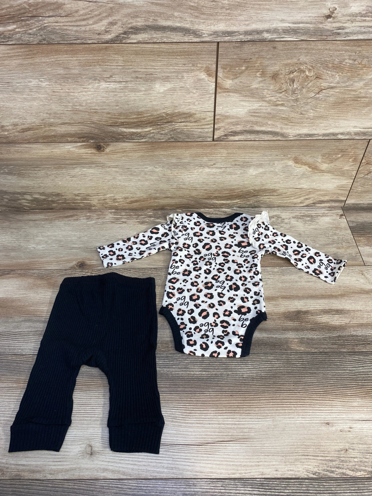 Leopard print baby bodysuit and black ribbed pants set on wood floor