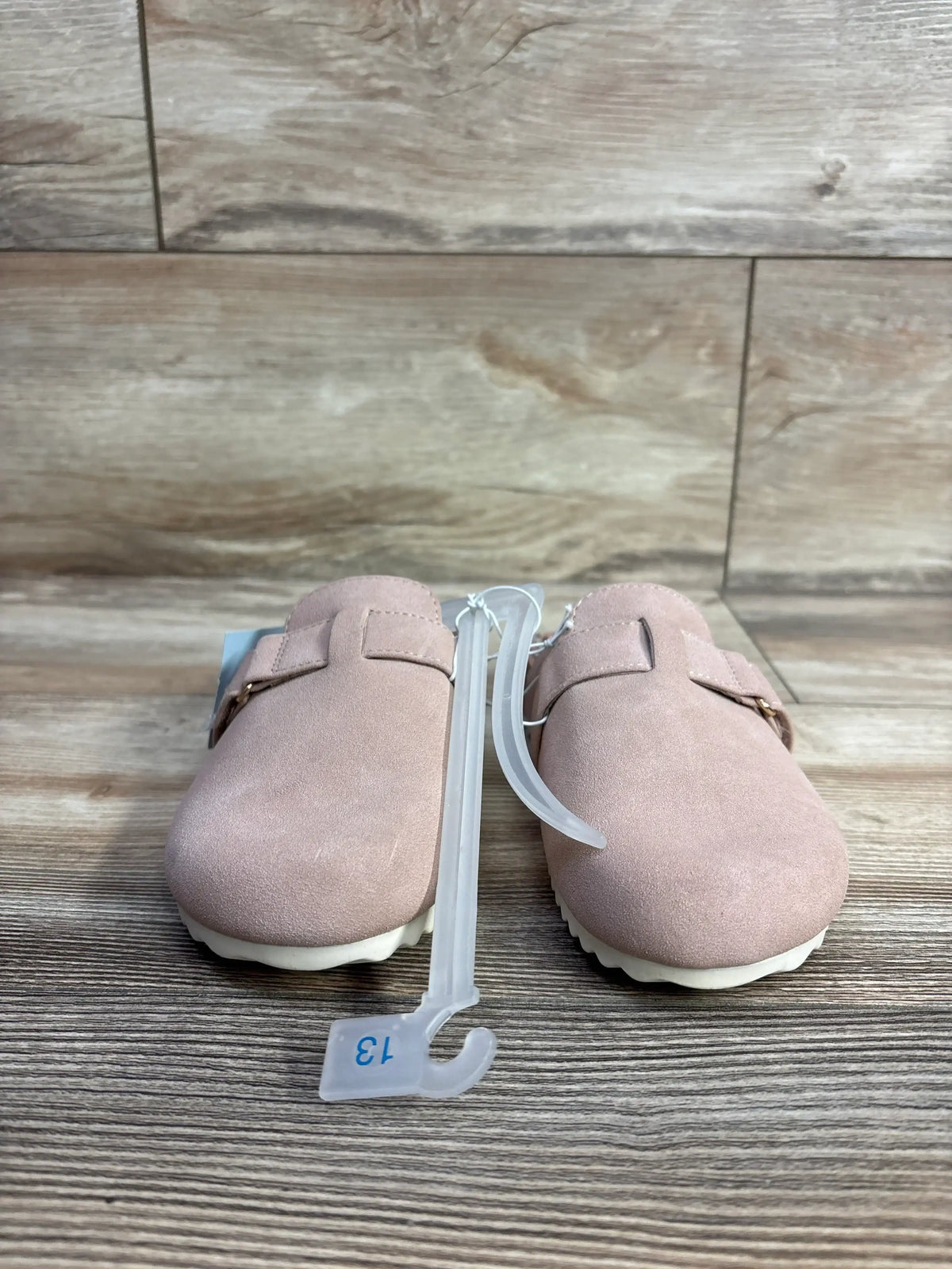 Pair of pink toddler shoes with white soles displayed on wooden floor, size 13 tag attached