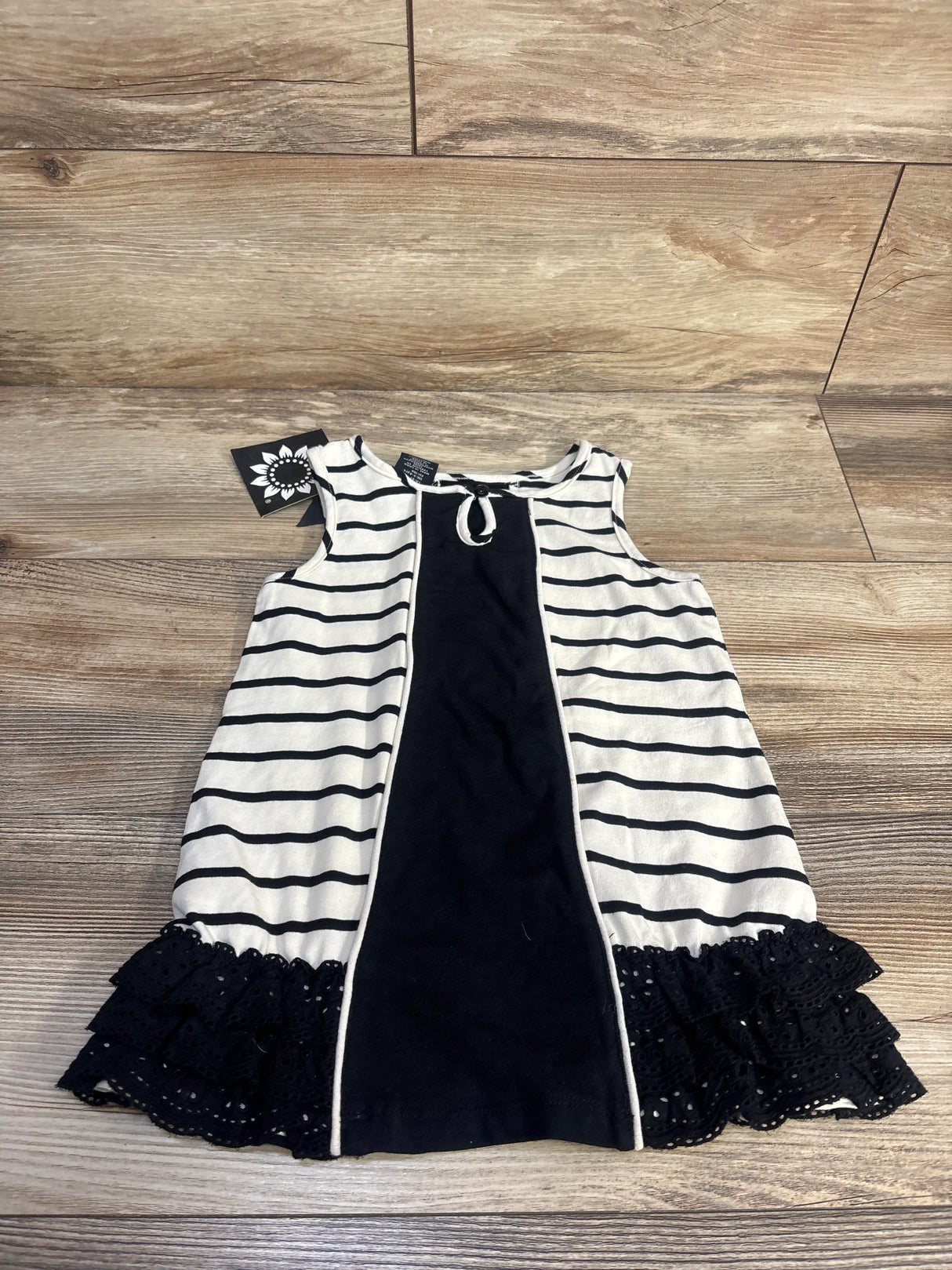 Front view of white sleeveless striped tunic in size 4T showcasing eyelet trim and shoulder bow on a wood floor