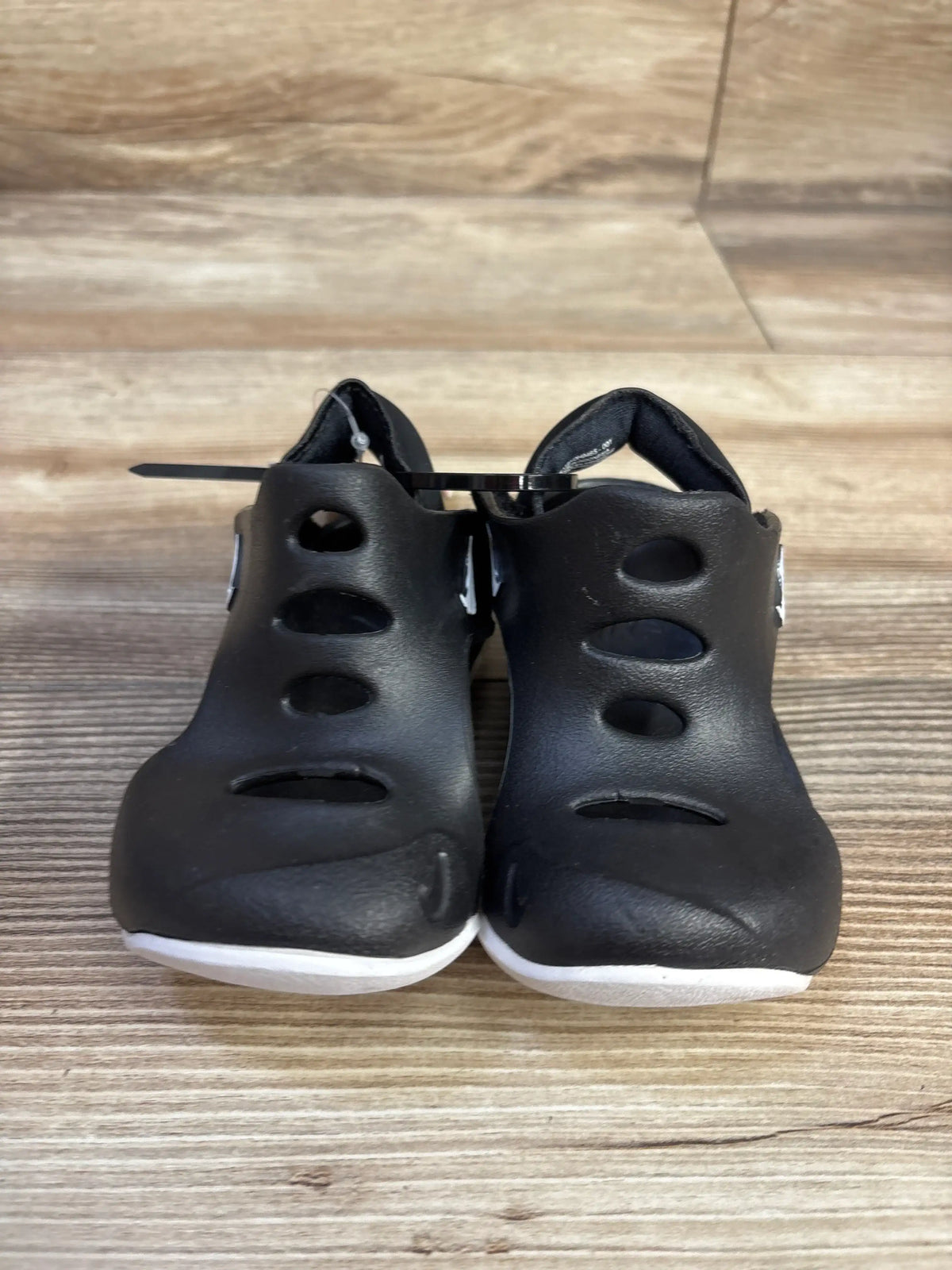Front view of Nike Sunray Protect 3 sandals in black showcasing ventilated open design and white rubber soles on a wood floor