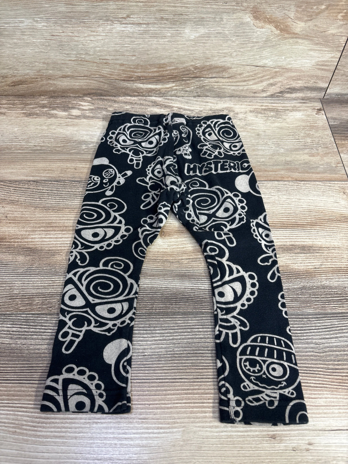 Black baby leggings with white cartoon pattern, gently used kids clothing on wood floor