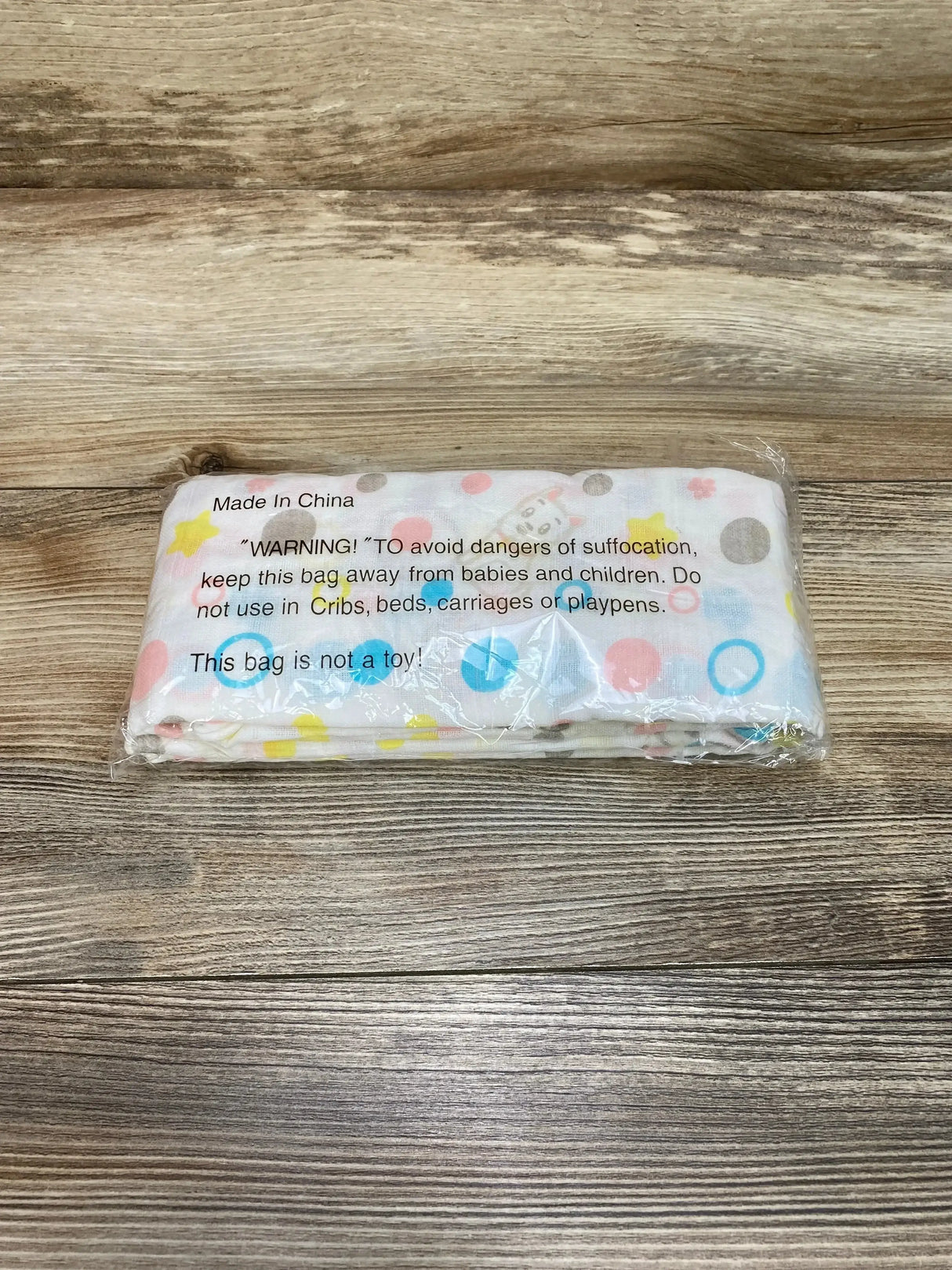 Top view of folded Cucumberries cotton muslin swaddle in clear plastic showing multicolor polka dots and paws on wood background