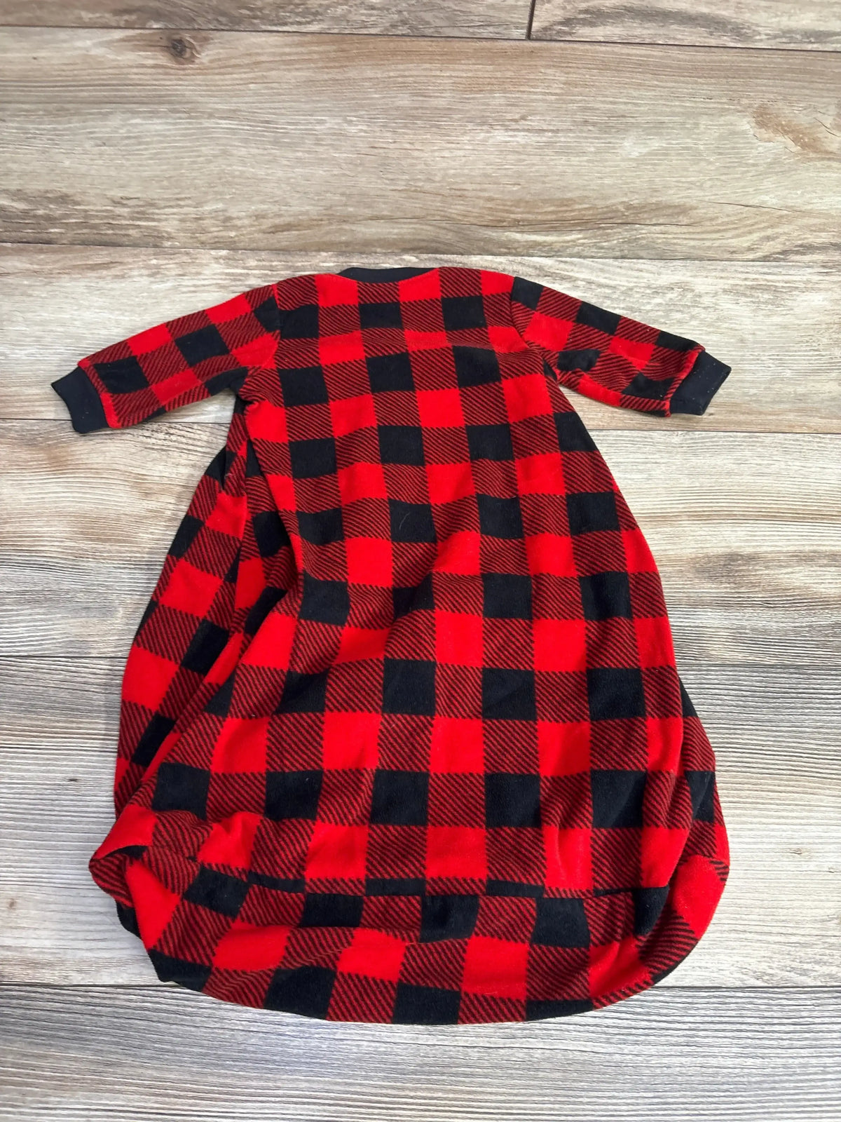 Red and black buffalo plaid baby sleep sack with long sleeves laid flat on wooden floor