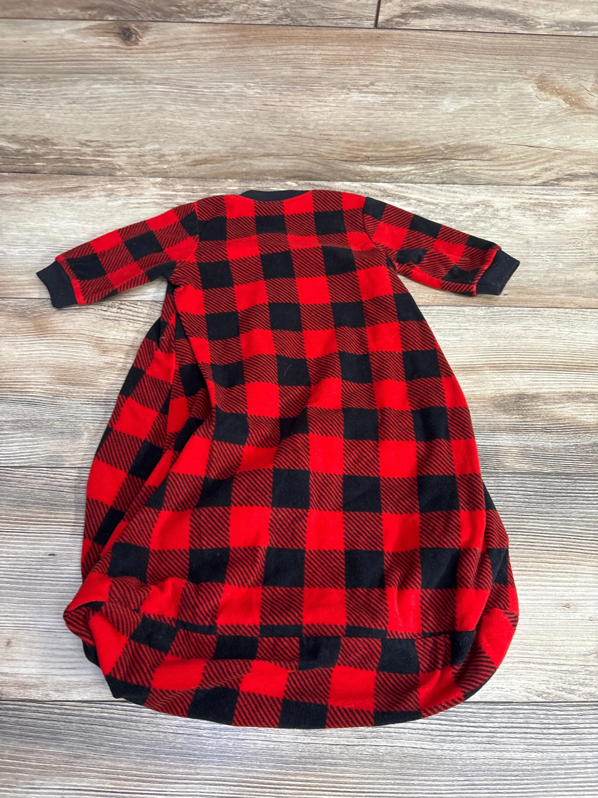 Red and black buffalo plaid baby sleep sack with long sleeves laid flat on wooden floor