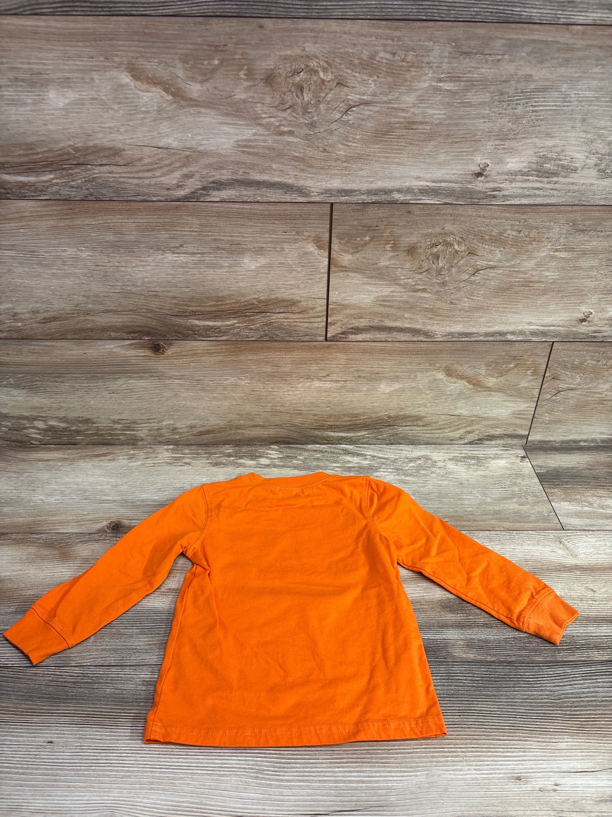 Back view of Carter’s Jack-O-Lantern shirt in orange, size 2T, showcasing long sleeves on a wood background