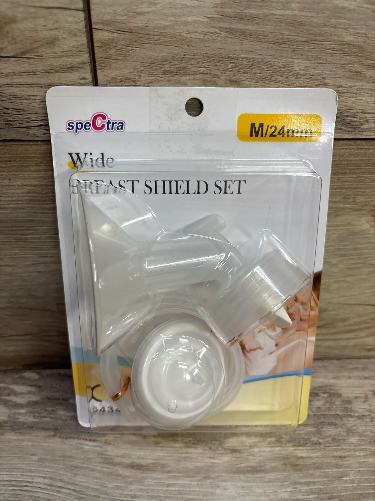 Front view of Spectra wide breast shield set M/24mm showing wide funnel and connectors in clear plastic packaging on wooden surface