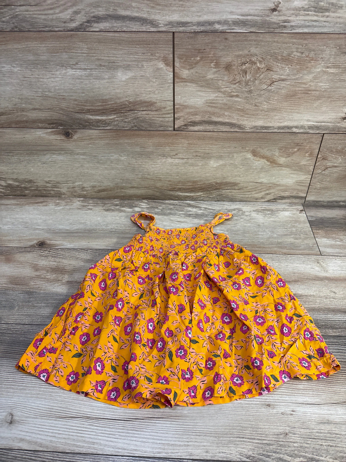 Top-down of Carter’s orange floral smocked viscose toddler dress (24M) showing smocked bodice and thin straps on wood floor