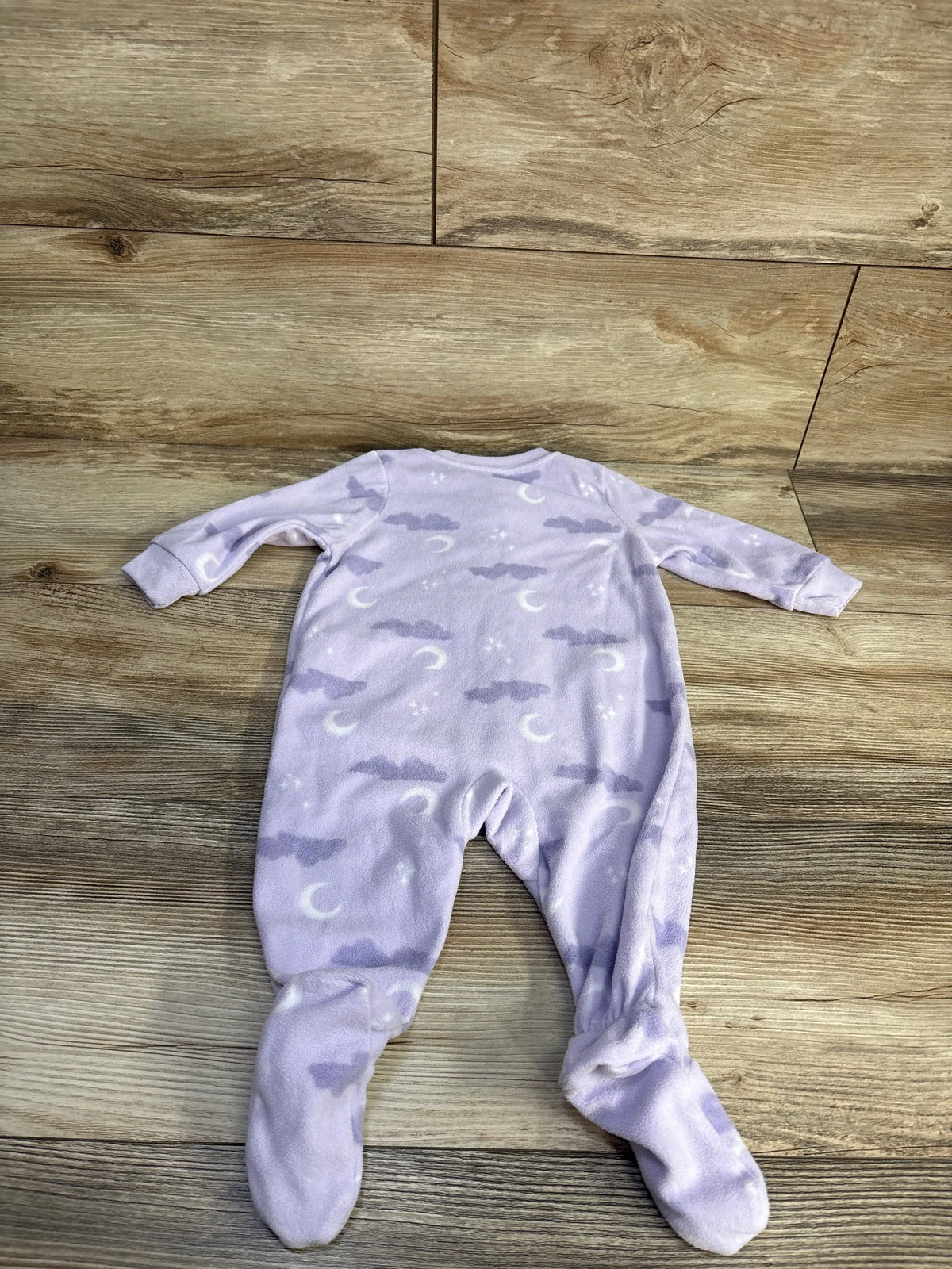 Front view of Carter’s purple blanket sleeper in size 6 months showcasing moon, cloud, and star pattern on a wood floor