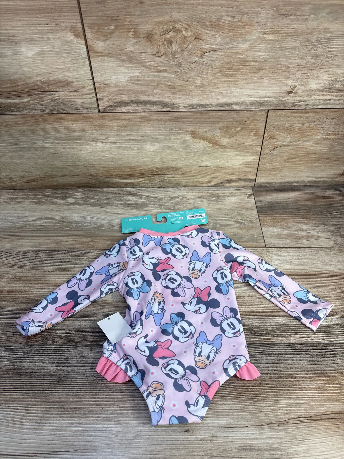 Front view of pink Minnie Mouse rash guard swimsuit with long sleeves and character print on a wood floor