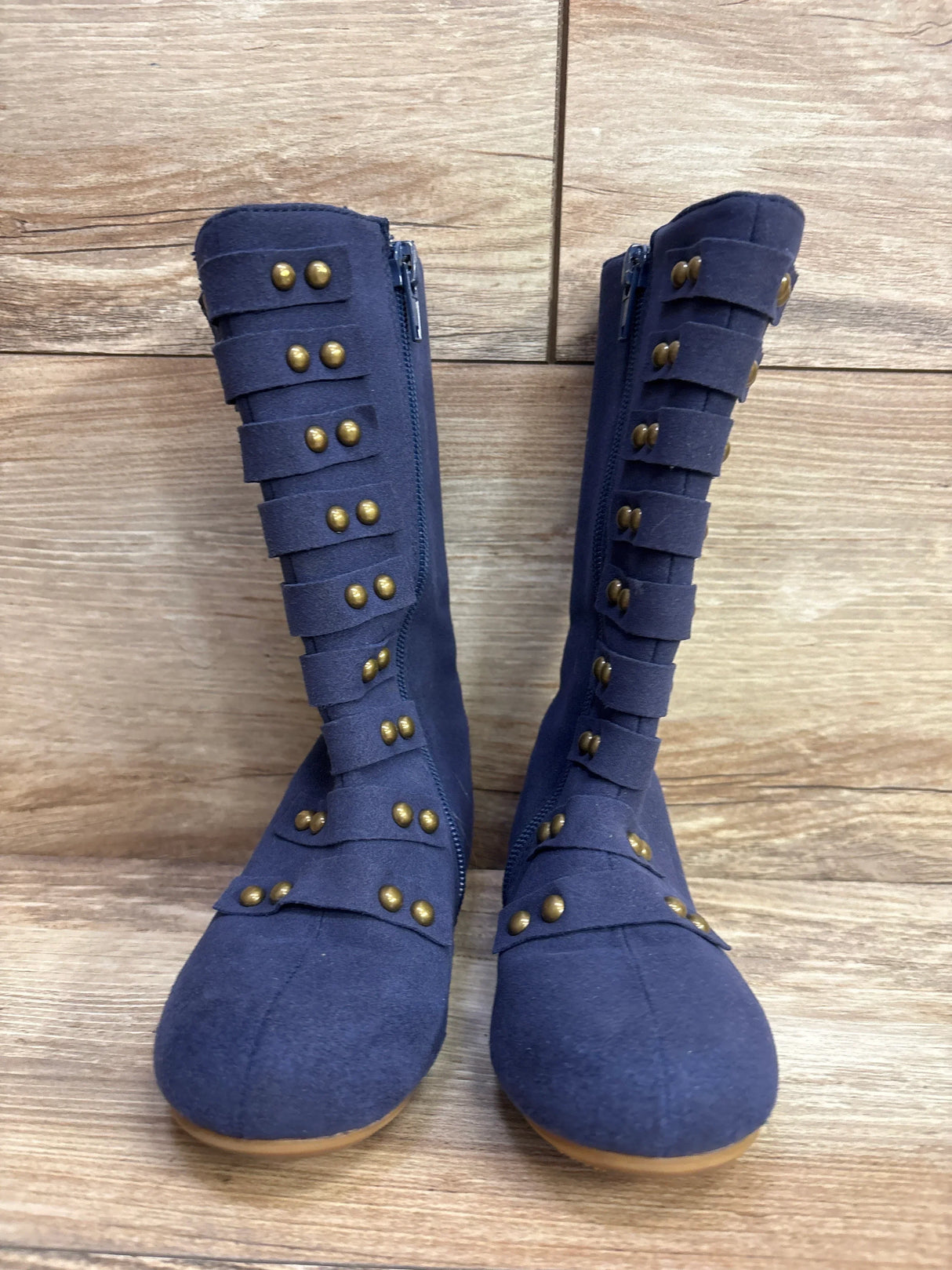 Pair of navy blue children's boots with brass studded straps on wooden floor