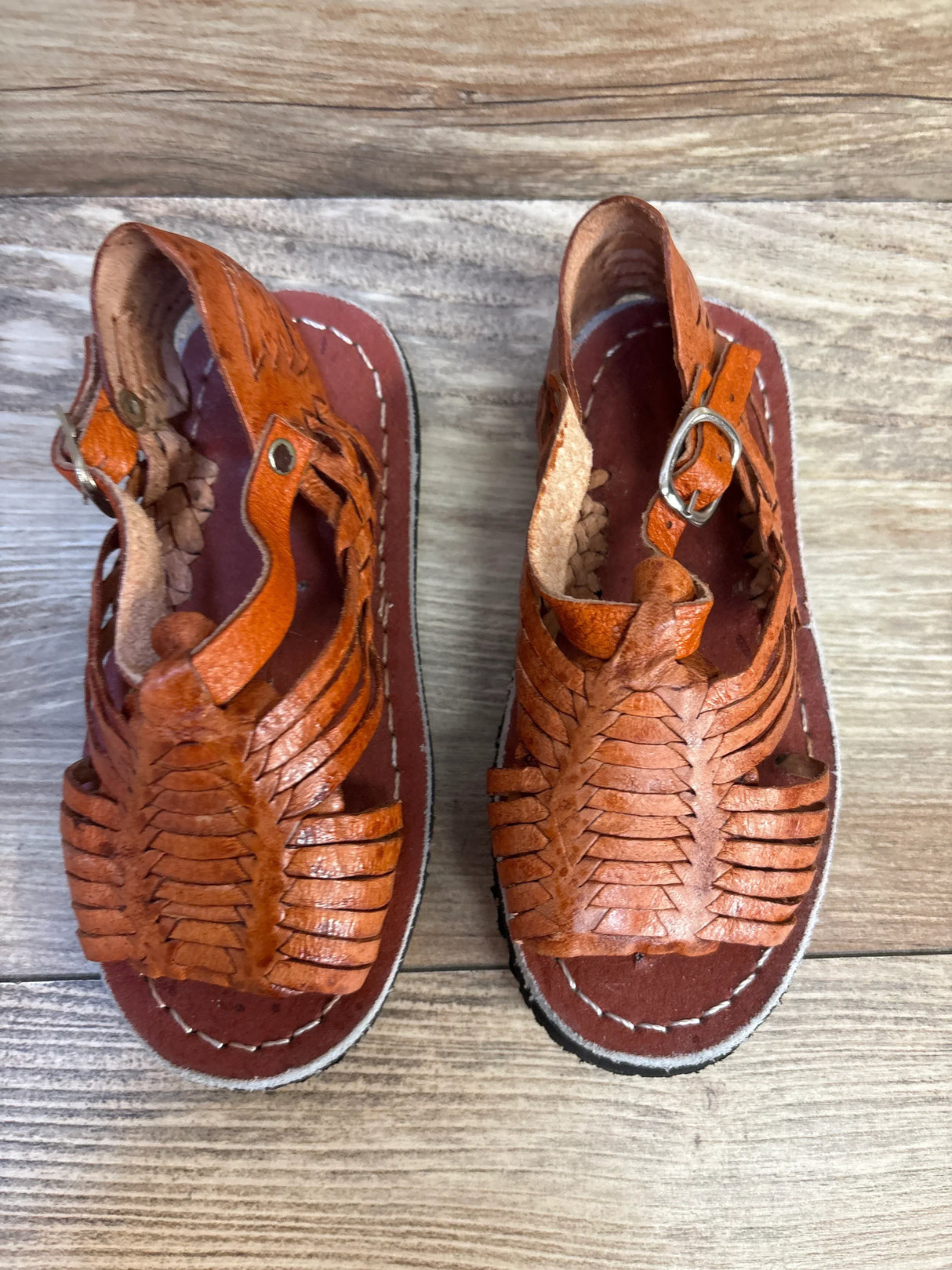 Brown leather kids huarache sandals with buckle closure on wooden floor
