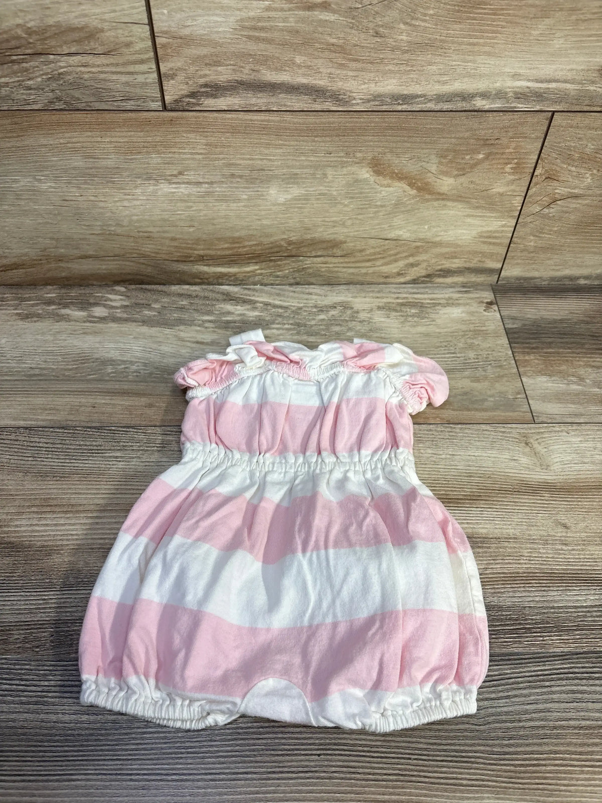 Top down view of a Ralph Lauren pink and white striped baby romper showcasing ruffled elastic collar and leg openings on a wood floor background