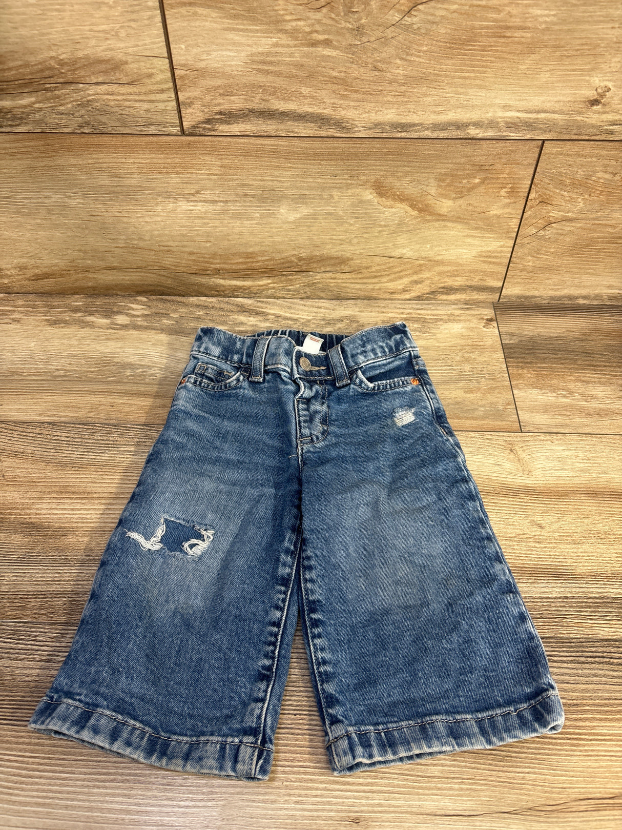 Flat lay of Cat & Jack distressed wide-leg jeans, front view showing faded blue denim and knee tear on wood floor background