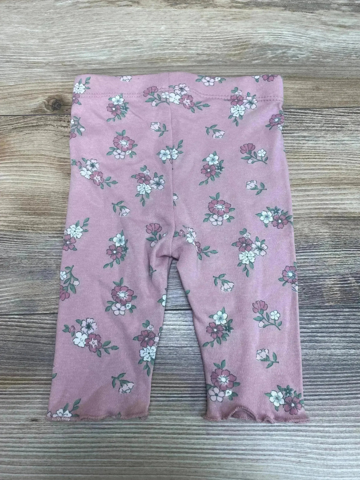 Front view of Tahari floral baby leggings size 0-3M showcasing mauve floral print and ruffled hems on wood