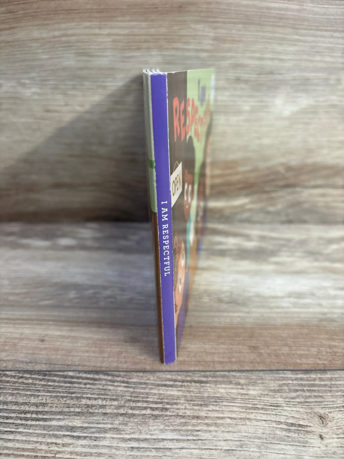 Side view of I Am Respectful lift-a-flap board book showing purple spine labeled I AM RESPECTFUL on wood surface