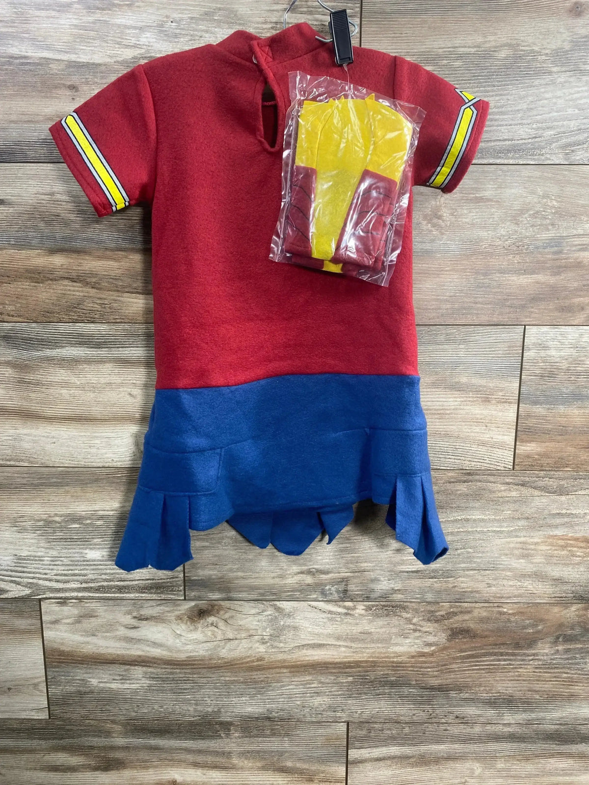 Top-down view of Justice League Wonder Woman costume set in red and blue with yellow accessories in a plastic bag on a wooden floor
