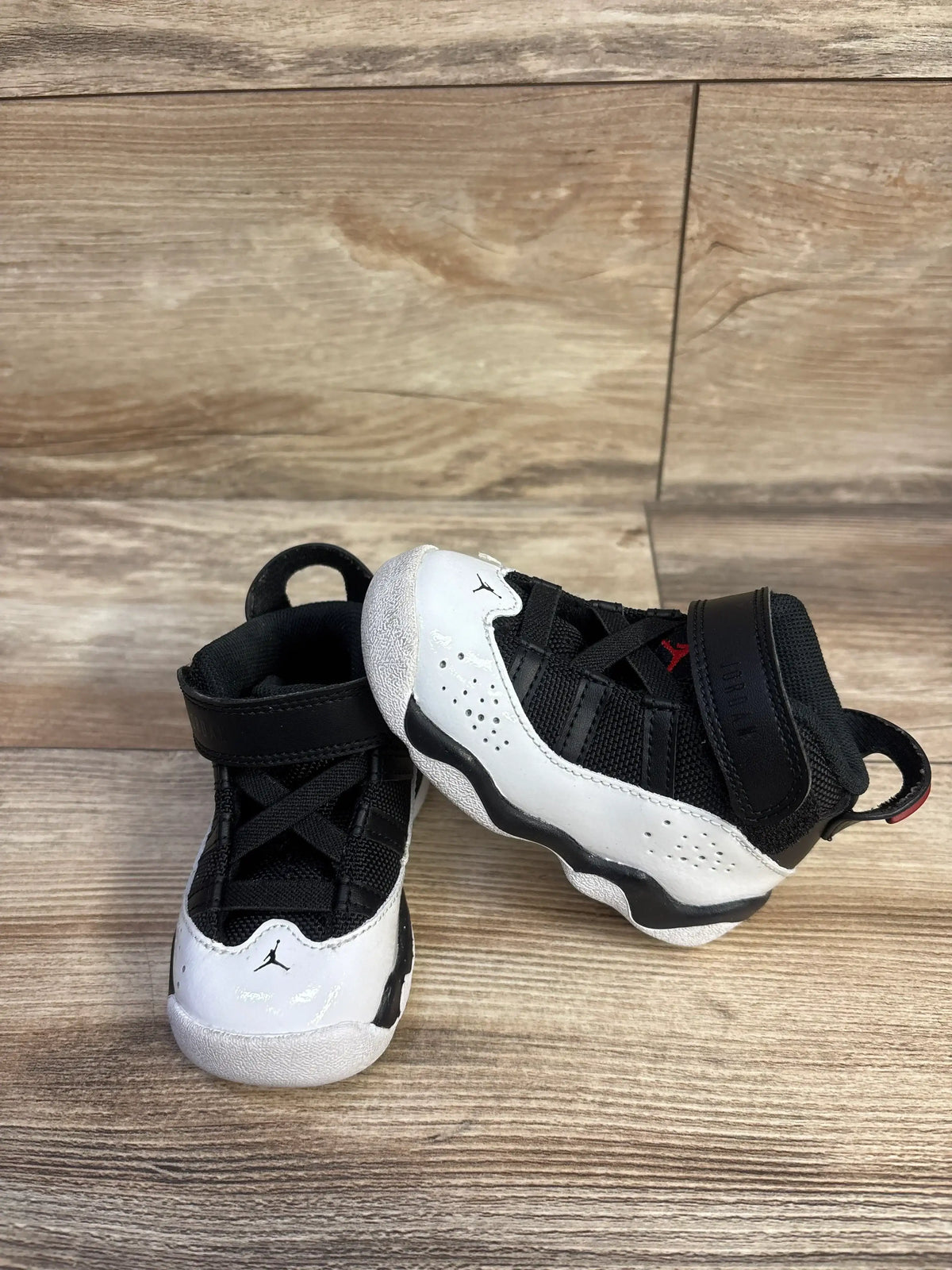 Three-quarter view of Air Jordan 6 Rings TD sneakers size 5c in black white and red with Jumpman logo on wood plank floor