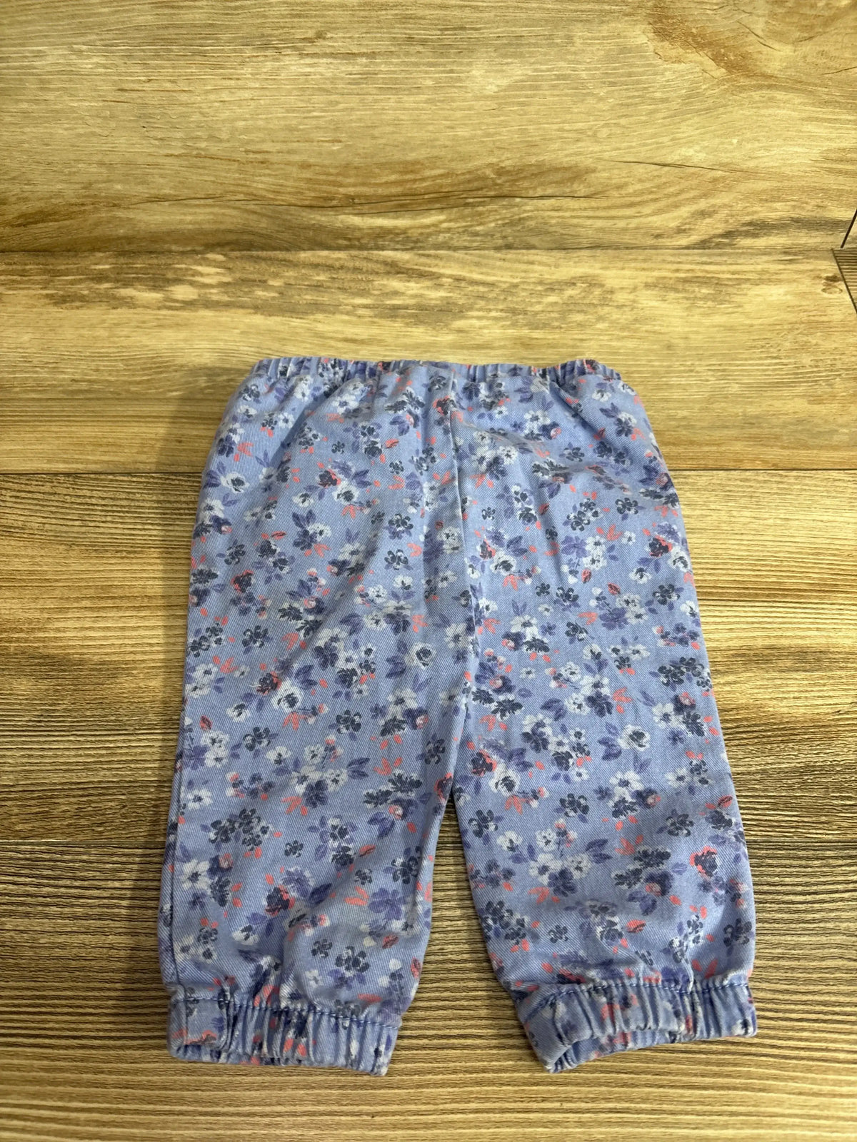Front view of Oshkosh blue floral print pull-on twill pants showcasing elastic waist and ankle cuffs on a wood surface