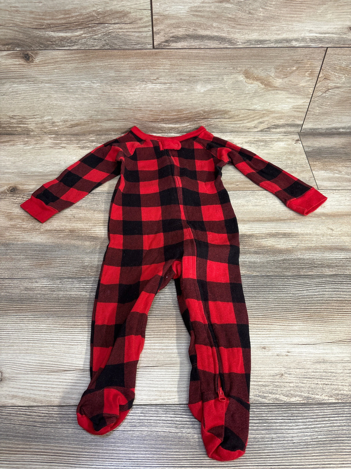 Red and black plaid baby footed sleeper with zipper on wood floor