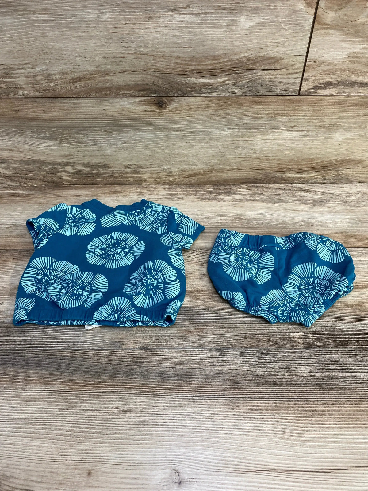 Flat lay of Carter's two-piece teal blue floral shirt and matching bloomers showing light blue flower print on wood