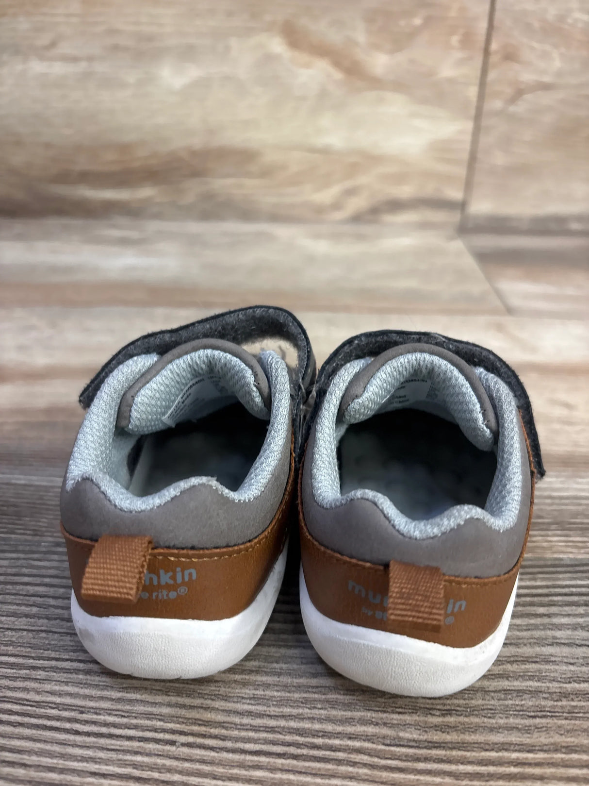 Rear view of Munchkin Miller toddler sneakers showing brown heel tabs, Velcro straps and white soles on wood floor