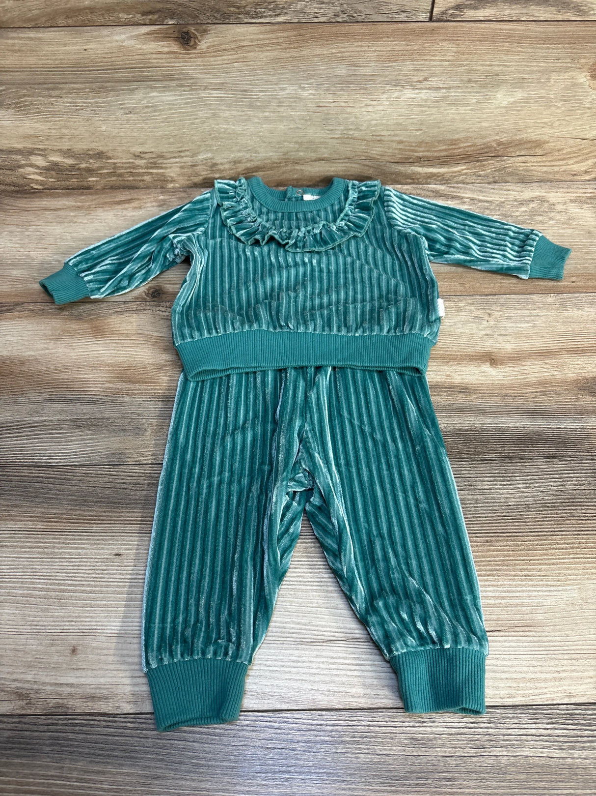 Green velvet toddler outfit with ruffled collar and ribbed cuffs on wood background