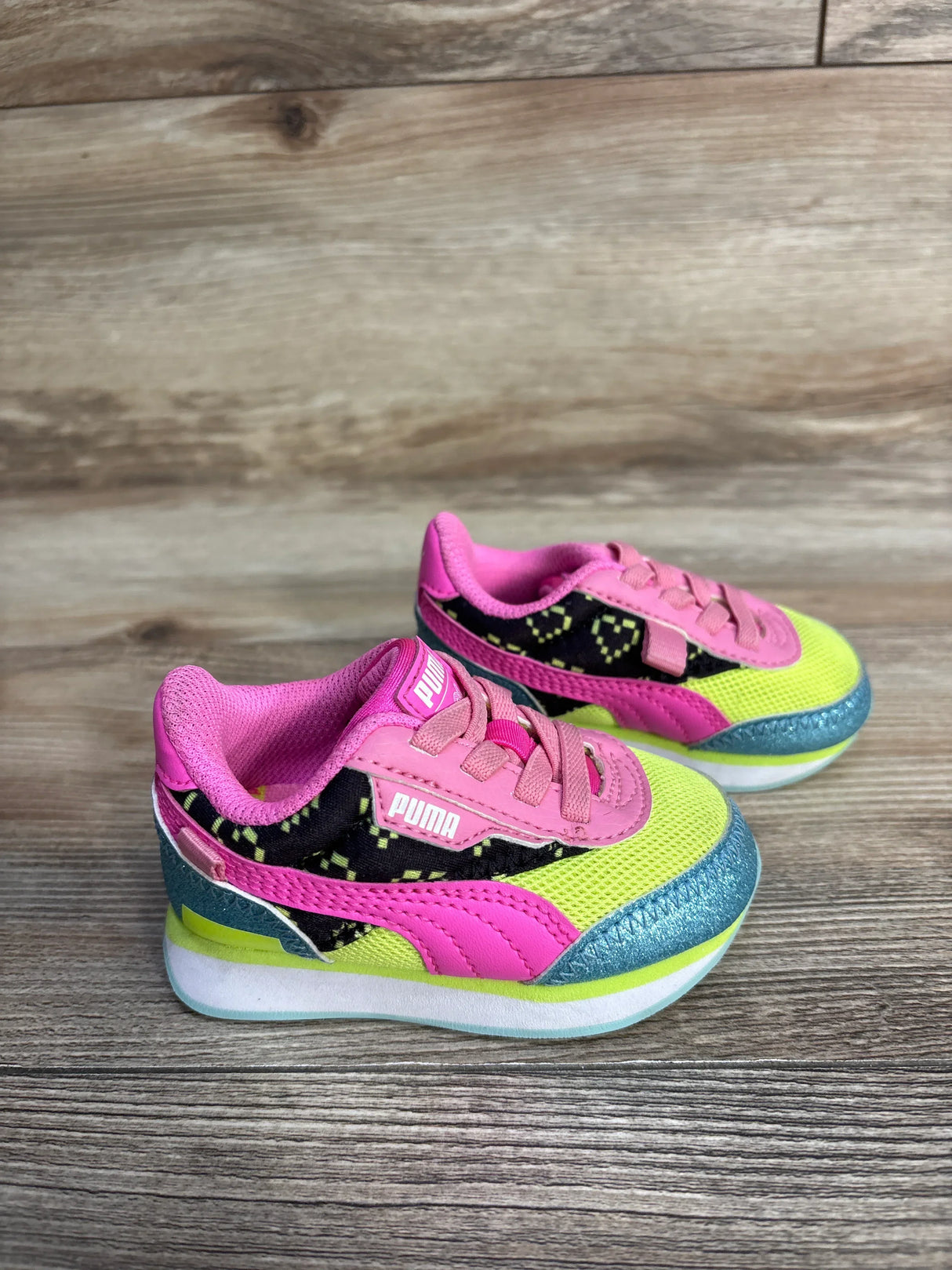 Pair of colorful Puma toddler sneakers in pink, yellow, and teal on wooden floor