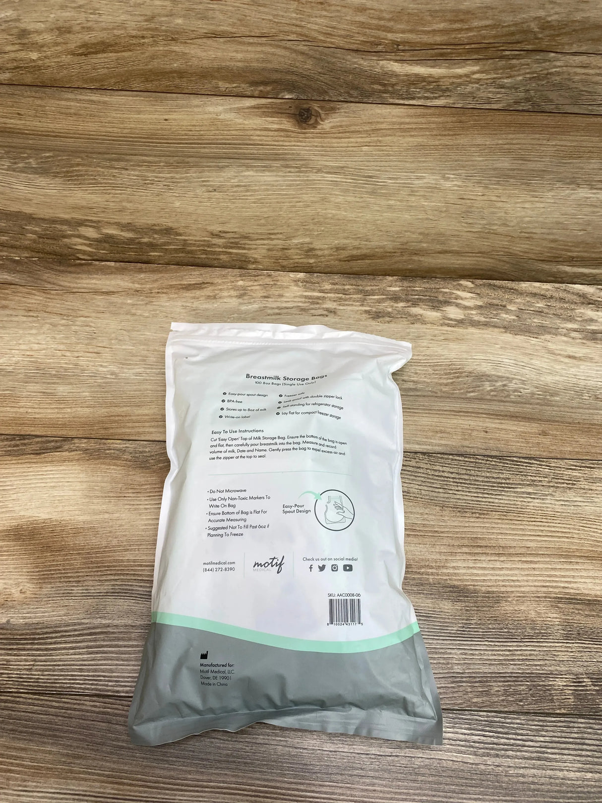 Rear view of Motif Medical breastmilk storage bags 100-count pack showing instructions and easy-pour spout icon on wood background