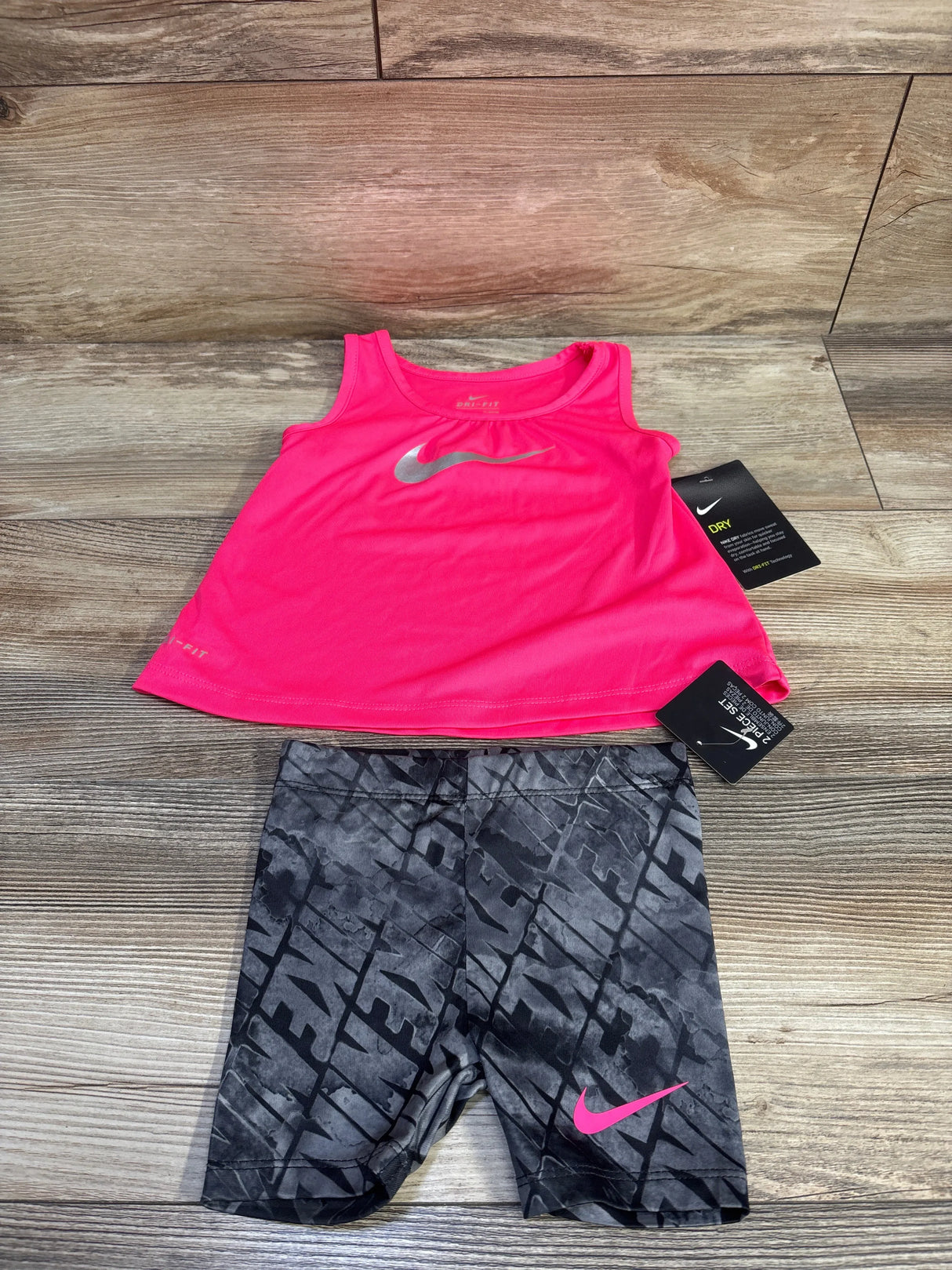 Flat-lay of Nike Dri-Fit tank and shorts showing hot pink tank with silver swoosh and gray shorts, pink swoosh on wood floor