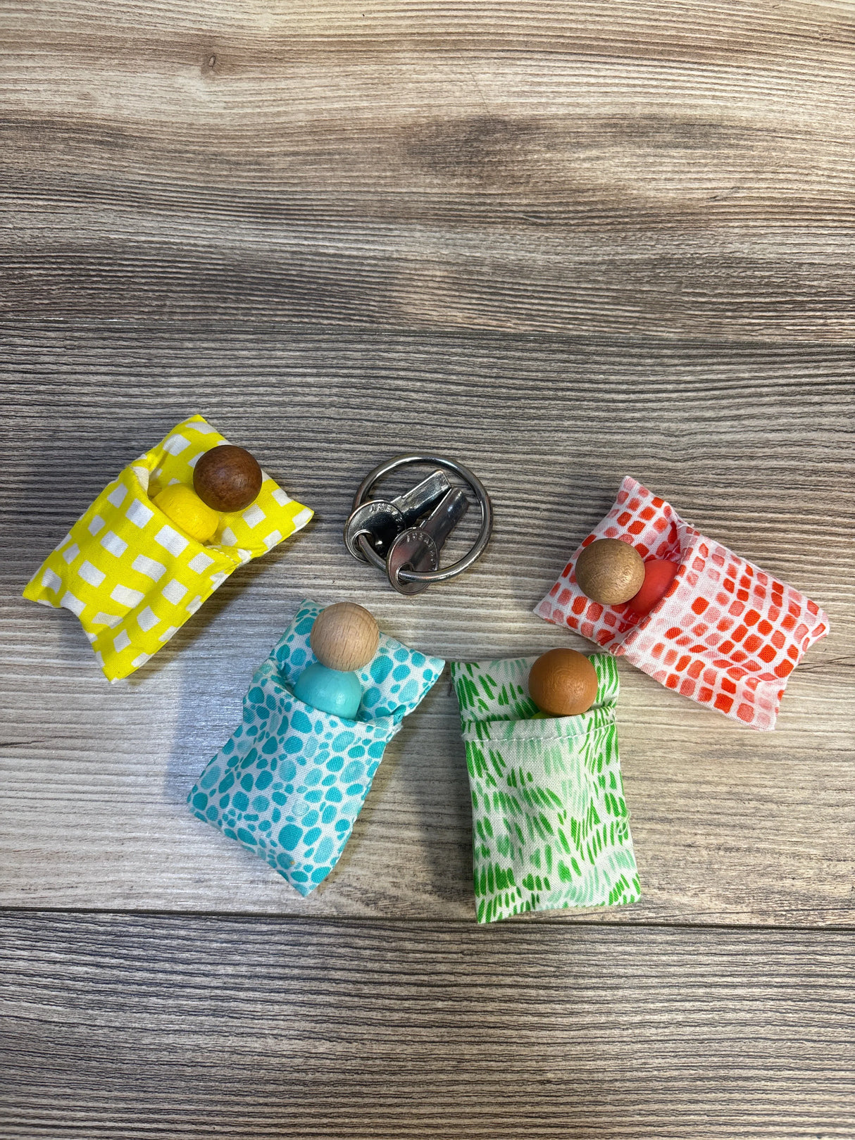 Colorful wooden peg dolls in patterned fabric beds on wood background, kid toy display