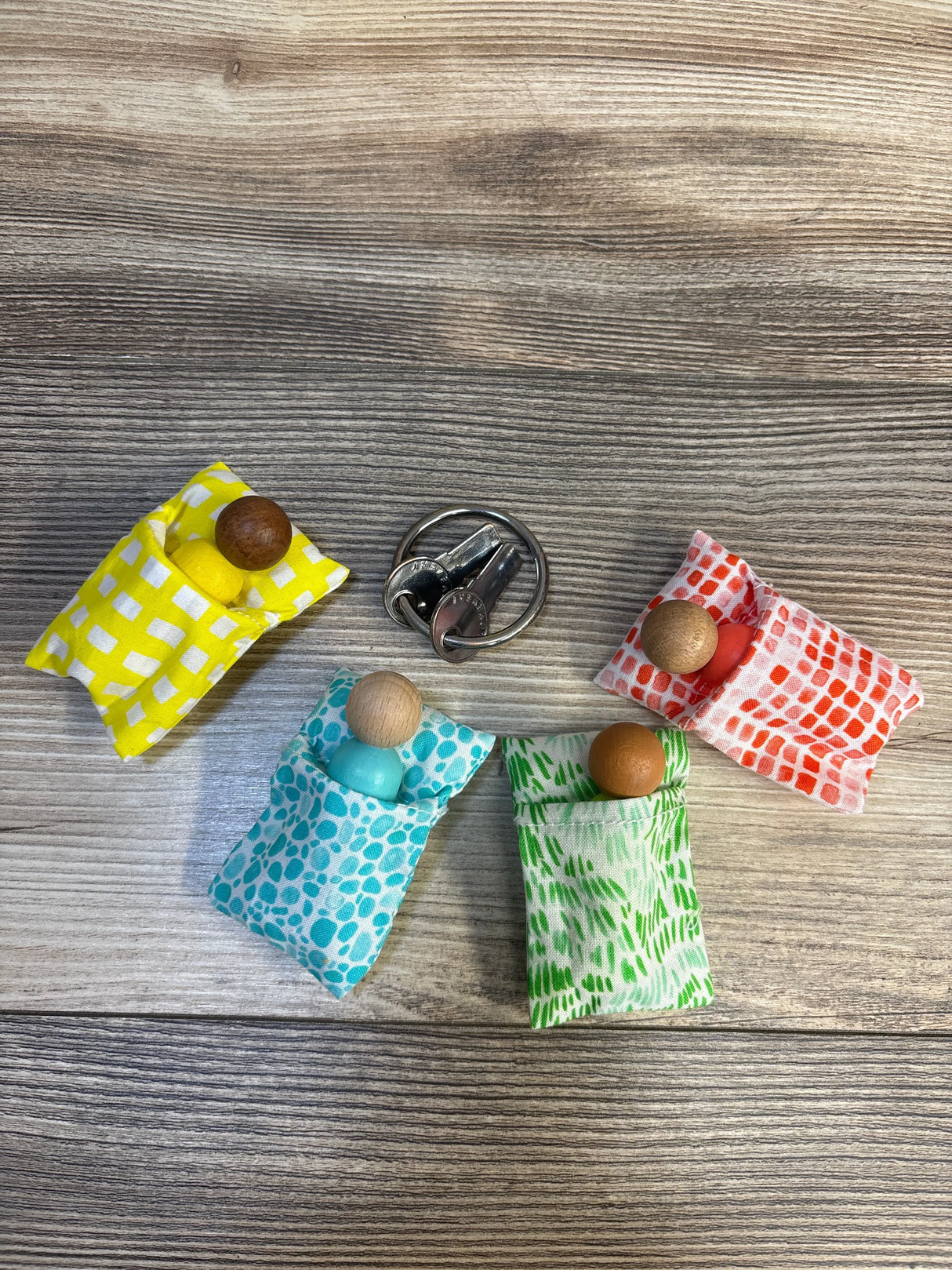 Colorful wooden peg dolls in patterned fabric beds on wood background, kid toy display