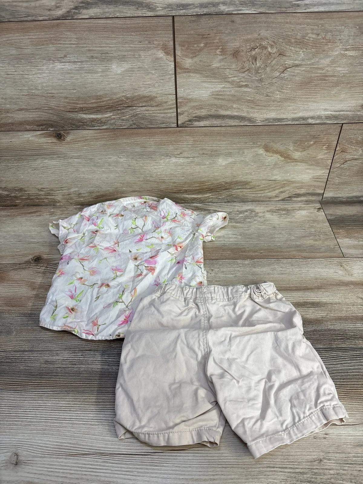 Flat lay of H and M two piece set with floral print short sleeve button up shirt and ivory shorts on wood plank floor