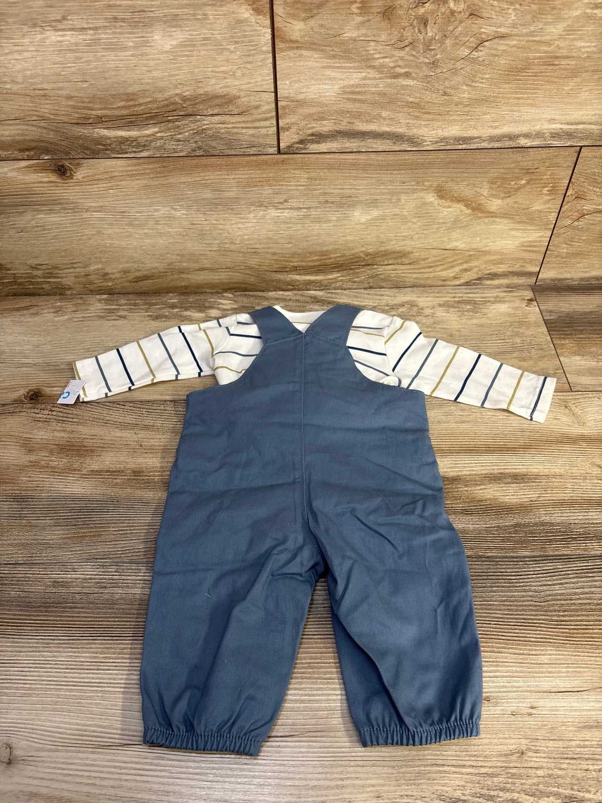 Flat-lay back view of white long-sleeve striped shirt and blue overalls set showing elasticized ankle cuffs on wood floor background