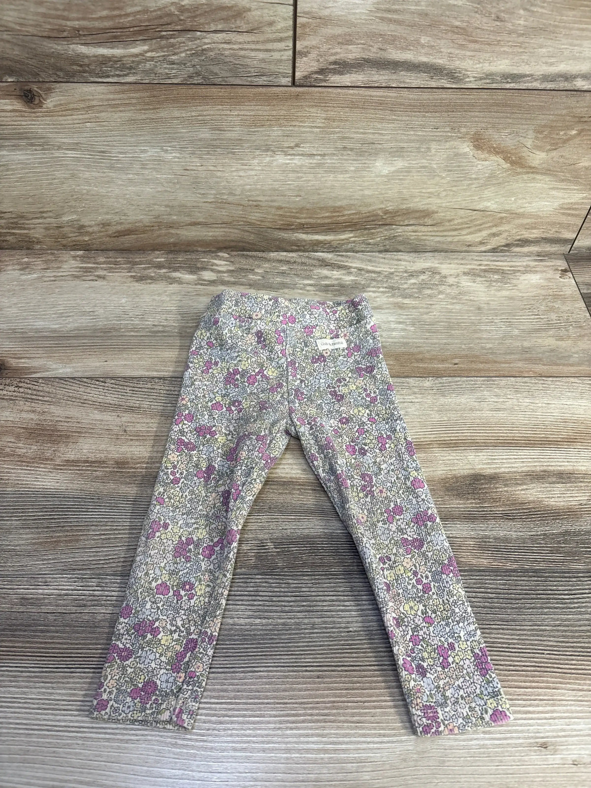 Flat lay front view of cream Zara ribbed leggings 18m showing small pink, purple and yellow floral print on wood background