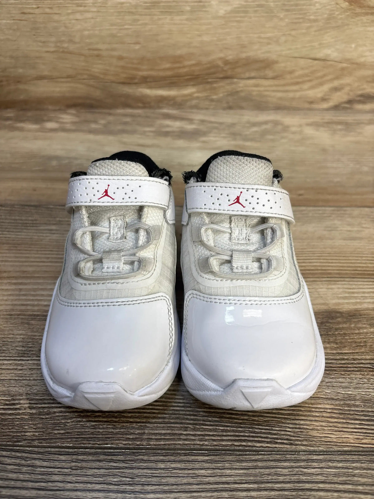 White toddler athletic sneakers with red accents, velcro strap, on wooden background