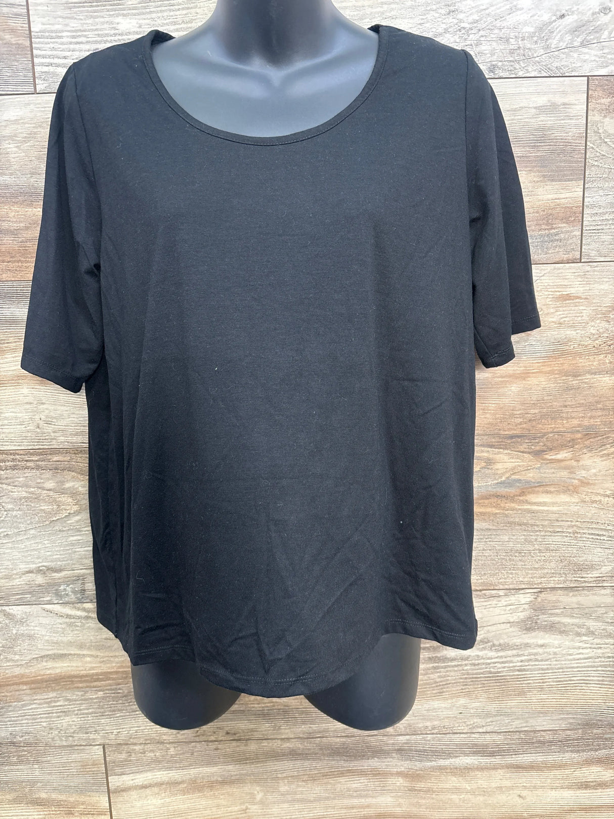 Plain black short sleeve t-shirt on mannequin against wood panel background