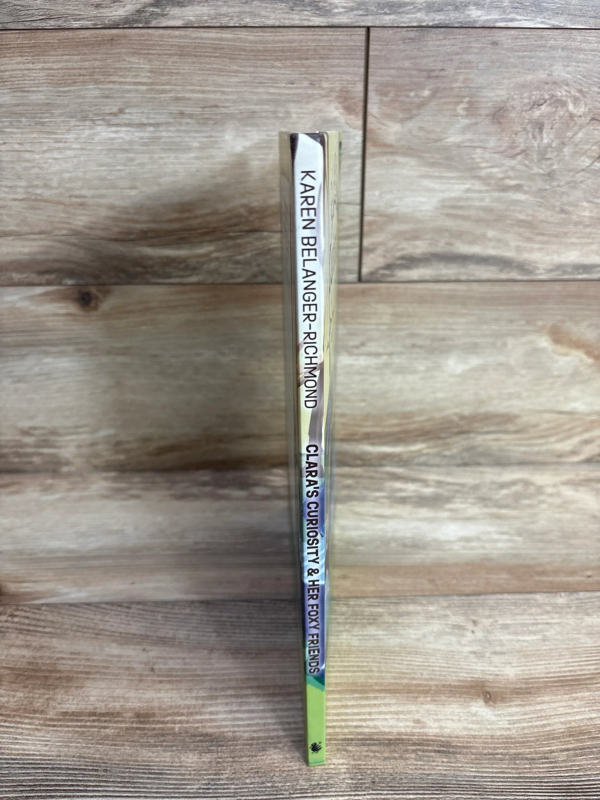 Spine of a children's book titled Clara's Curiosity & Her Foxy Friends by Karen Belanger-Richmond on wooden surface