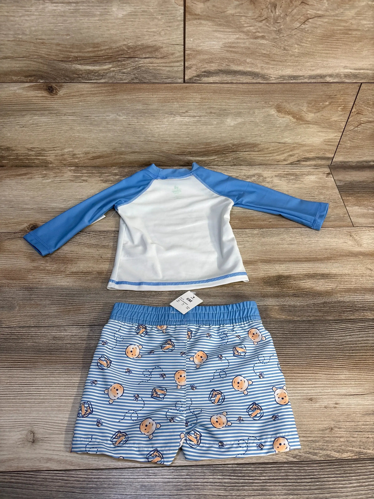 Blue and white baby swim set with Winnie the Pooh print, size 6M, laid on wood floor