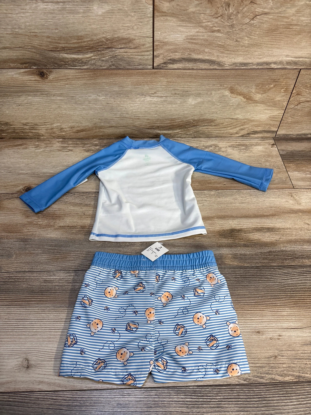 Blue and white baby swim set with Winnie the Pooh print, size 6M, laid on wood floor