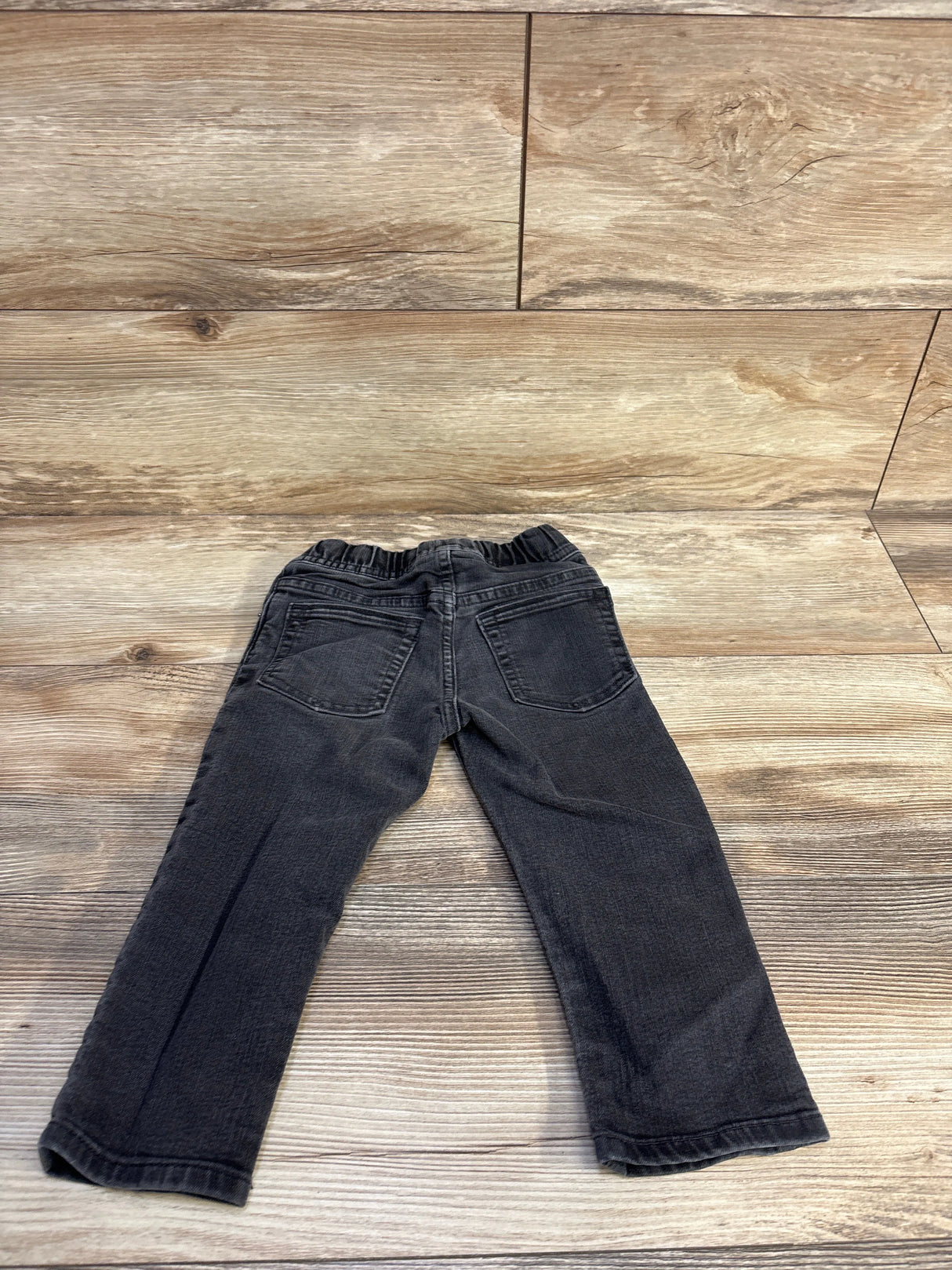 Back view of Baby Gap grey denim toddler jeans showing elastic drawstring waistband and back pockets on wood background