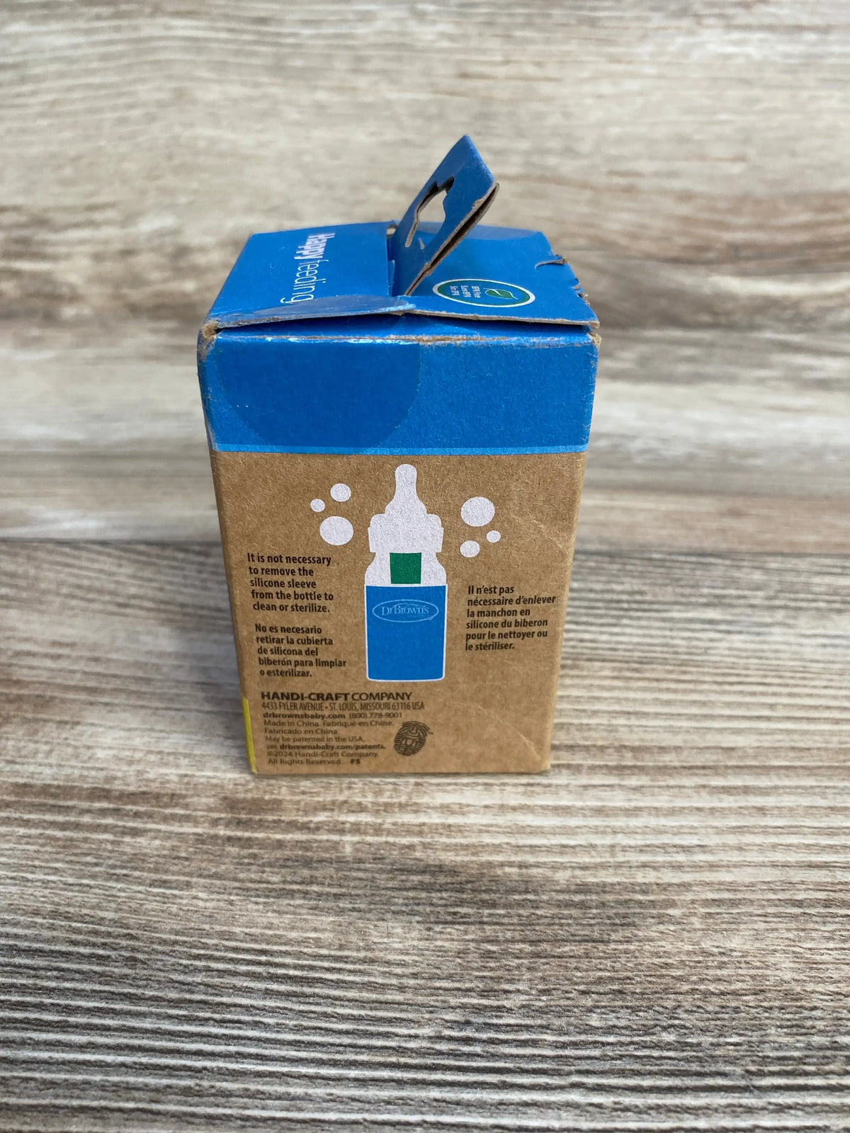 Front view of Dr. Brown’s Options+ 4 oz glass baby bottle sleeve in box showcasing glow-in-the-dark graphic on wood surface