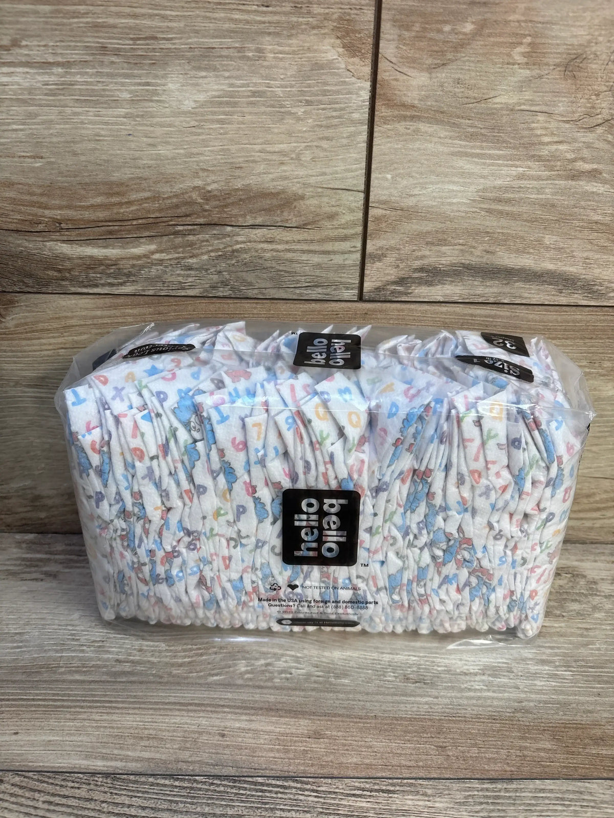 Front view of Hello Bello size 1 diapers (32 ct) showing printed pattern and clear plastic packaging on wood background