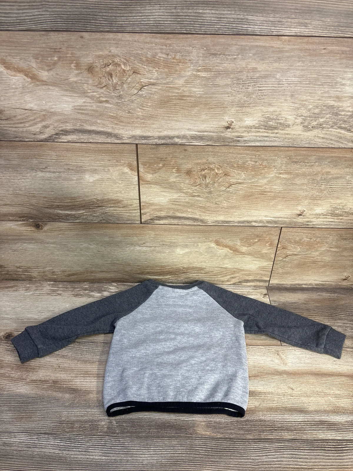 Front view of Reebok grey pullover sweatshirt, size 18 months, showcasing contrasting raglan sleeves on a wood-grain background