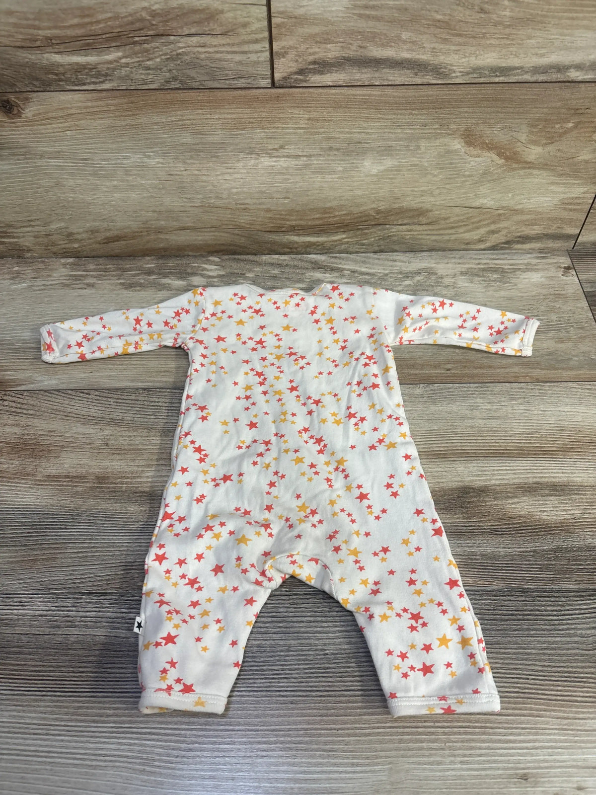 Front view of Molo Fenez star print coverall in cream and newborn size showcasing red and yellow stars, laid flat on wood