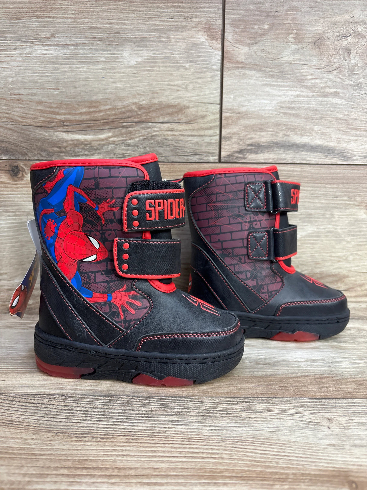 Kids black and red Spider-Man winter boots with velcro straps and web graphics on wood floor