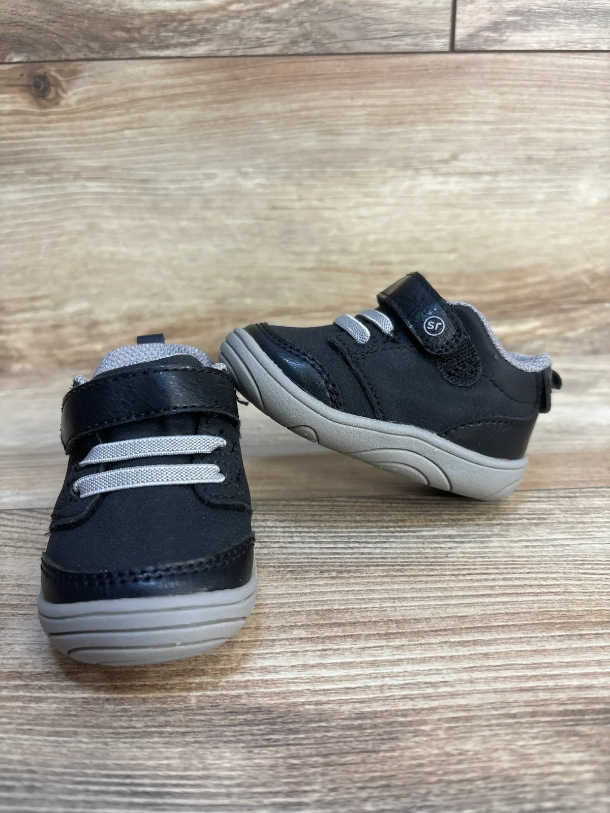 Black and gray toddler sneakers with velcro strap and rubber soles on wood background